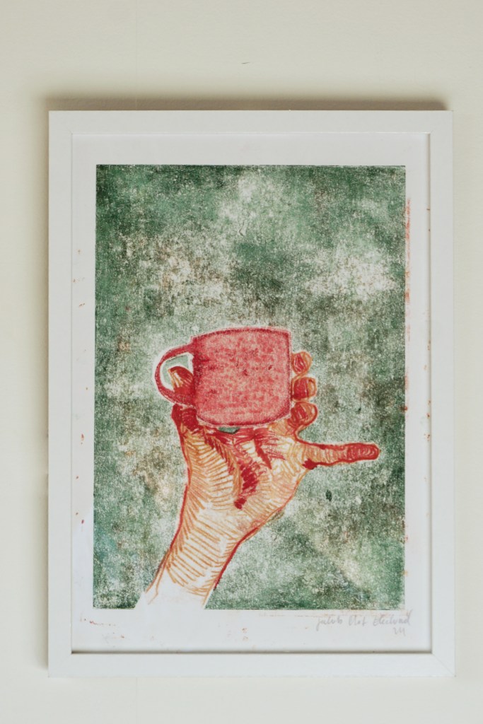 Inramat konstverk, kaffekopp och hand.