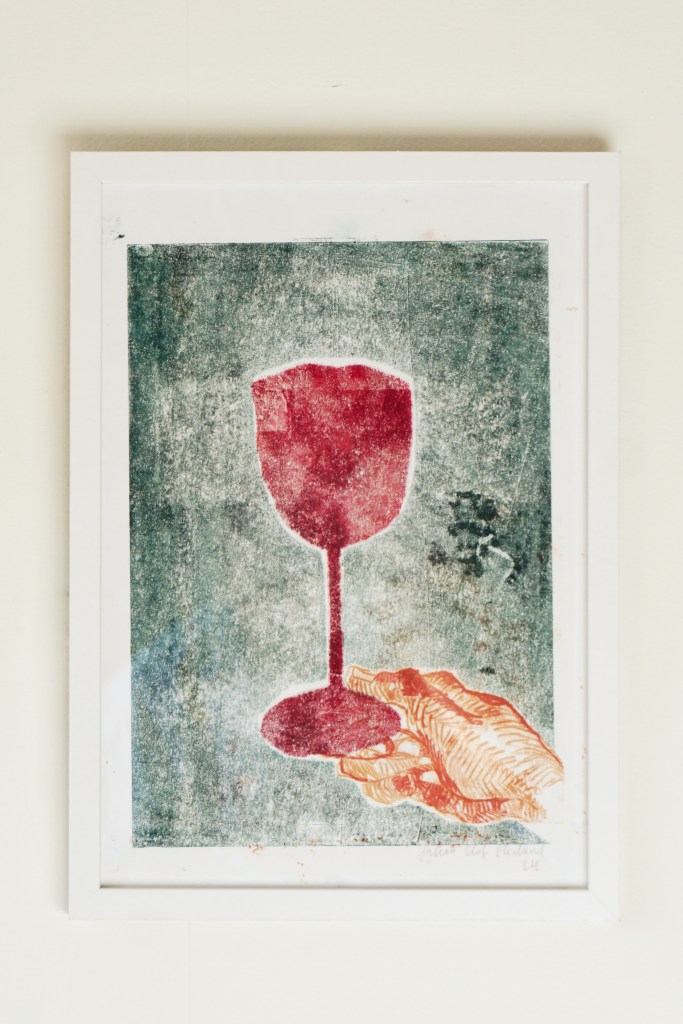 Inramat konstverk, vinglas och hand.